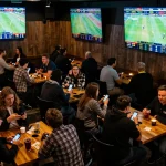 Engaging patrons in a sports bar actively placing bets as they analyze soi keo odds on large screens
